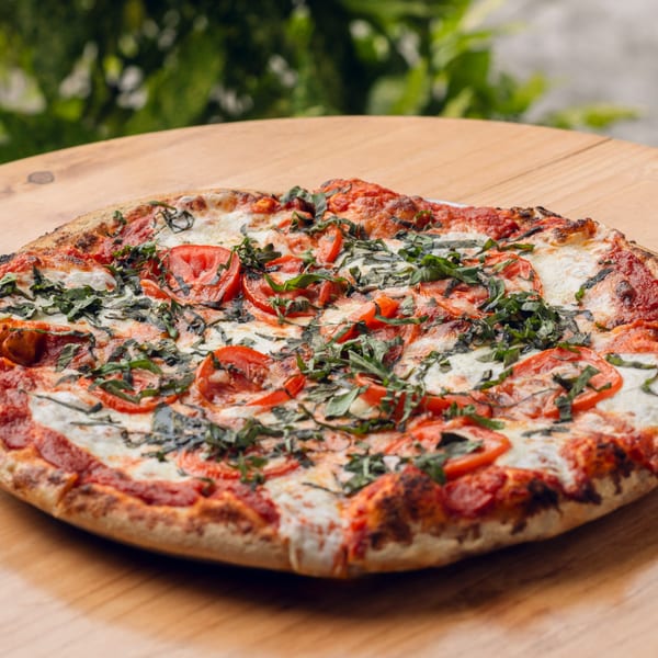 A whole Margherita pizza with fresh tomatoes, mozzarella, and basil on a wooden table.