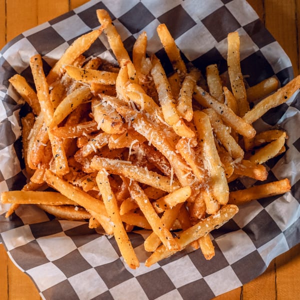 Golden french fries seasoned with herbs and parmesan cheese, served in a checkered paper-lined basket.