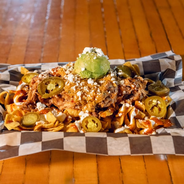 Loaded nachos with pulled pork, cheese sauce, jalapeños, cotija cheese, and a scoop of guacamole.